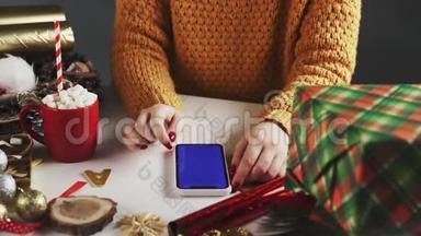 女士使用智能手机与Chroma键，点击，滑动，滚动向上。 白色桌子上的圣诞装饰